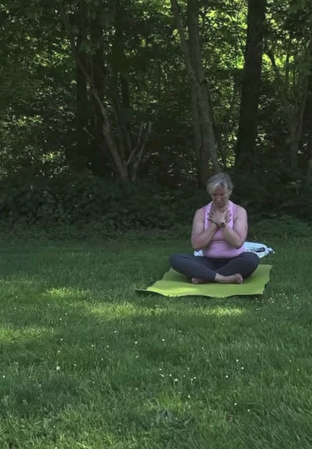 Frau sitzt ruhig in Meditation auf einer Yogamatte am Waldrand